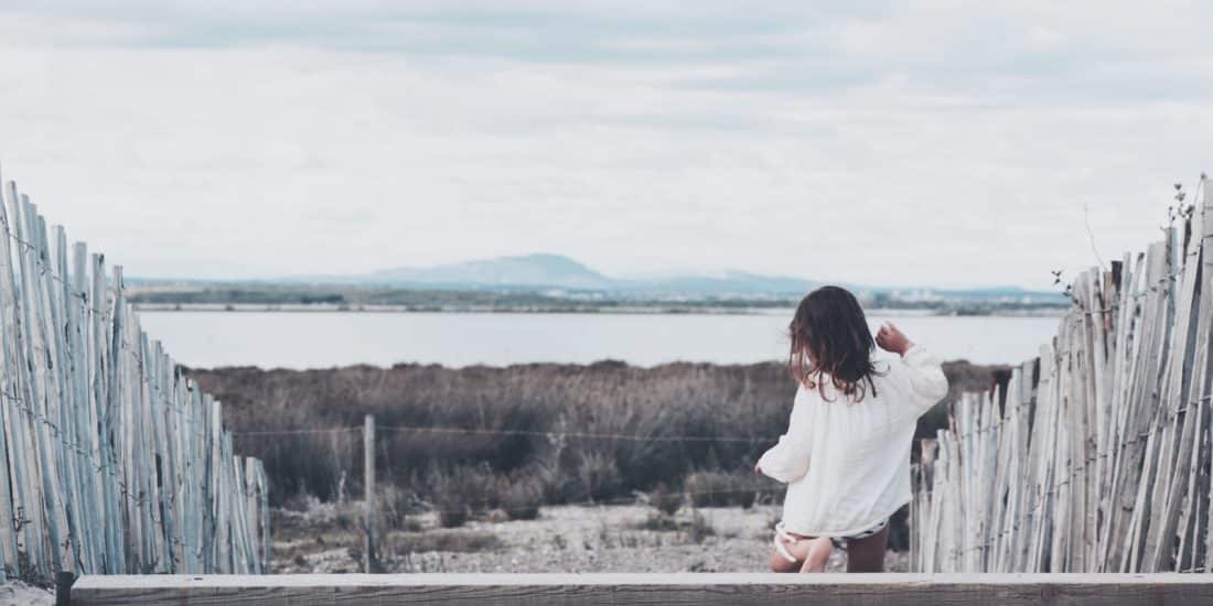 girl stepping down on wooden steps with wooden fence towards brown grassfield