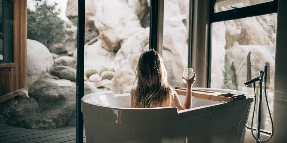 woman in white bathtub holding clear drinking glass